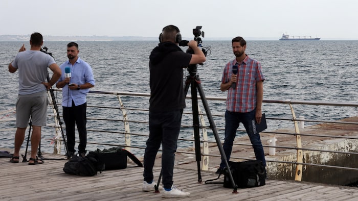 Des journalistes travaillent devant le navire qui quitte le port.