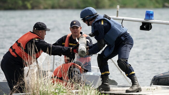 Des hommes déchargent une mine d'un bateau, près d'un lac. 