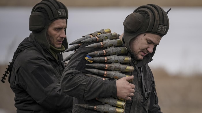 Un soldat en aide un autre à mettre des munitions sur son épaule.