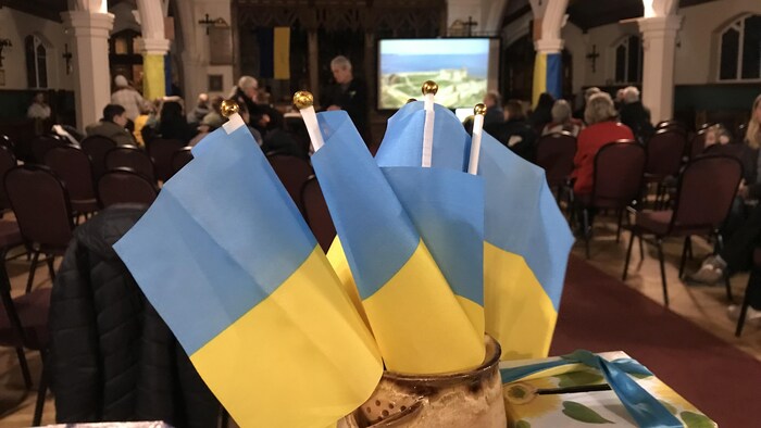 Des drapeaux ukrainiens. En arrière-plan, des gens assis dans une église. 