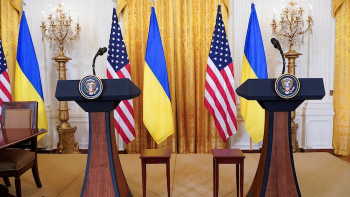 Une salle vide avec des lutrins et des drapeaux américains et ukrainiens.