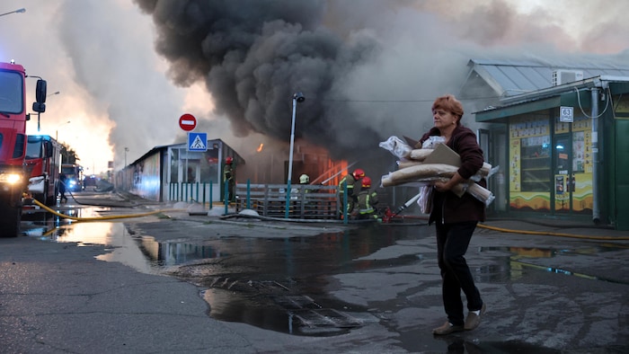 Une femme transporte des objets récupérés dans le marché aux livres ravagé par les flammes, tandis que les secouristes ukrainiens s'efforcent d'éteindre un incendie déclenché par une frappe russe à Kiev le 16 août 2026, dans le contexte de l'invasion russe de l'Ukraine.
