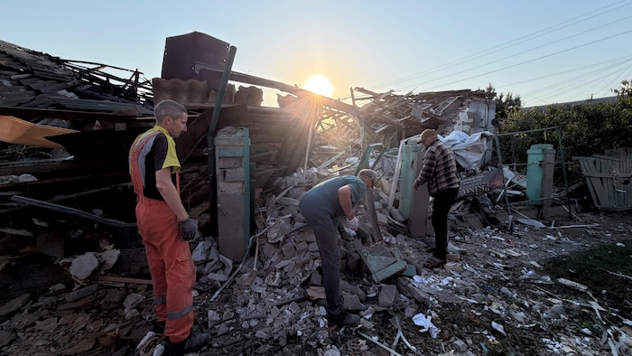 Trois personnes se tiennent parmi les décombres d'une maison.