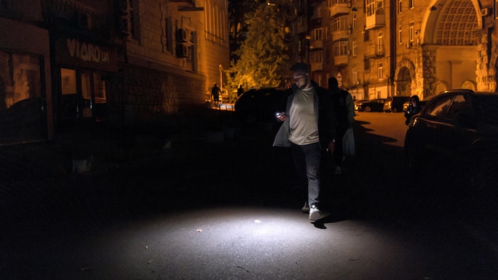 Un homme utilise la lampe torche de son téléphone alors qu'il marche dans une rue sombre lors d'une panne d'électricité partielle, au milieu de l'attaque russe contre l'Ukraine, à Kiev, en Ukraine, le 16 mai 2024.