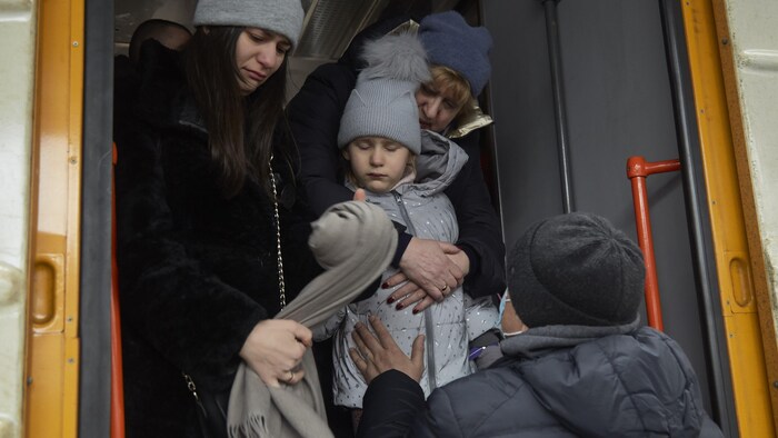 Un homme tient sa fille à la porte d'un train, sous les yeux triste de sa femme.