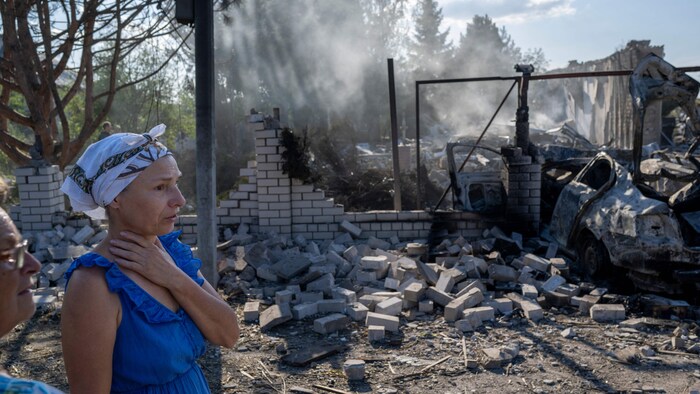 Une femme devant un bâtiment détruit.