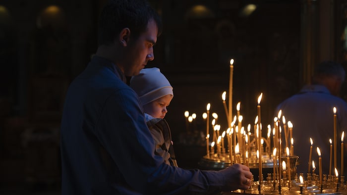 Un père et son enfant allument des bougies alors qu'ils prient dans une cathédrale.