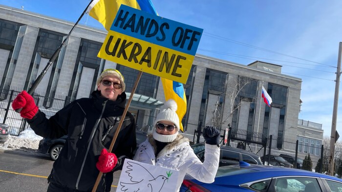 Deux personnes posent avec une affiche où il est écrit, en anglais, de laisser l'Ukraine tranquille.