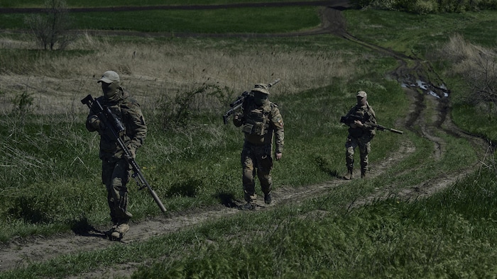 Des soldats ukrainiens munis d'armes de précision marchent sur un chemin de terre.