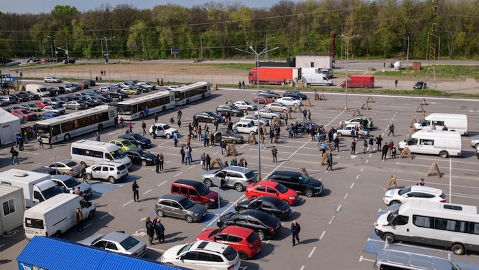 Vue aérienne d'un stationnement comprenant des dizaines de voitures et de nombreuses personnes. 