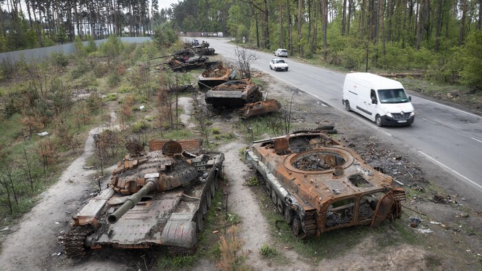 Des tanks détruits et carbonisés en bordure d'une route.