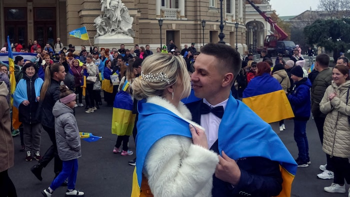 Un couple s'embrasse. Sur les épaules de l'homme et de la femme est drapé un drapeau ukrainien.