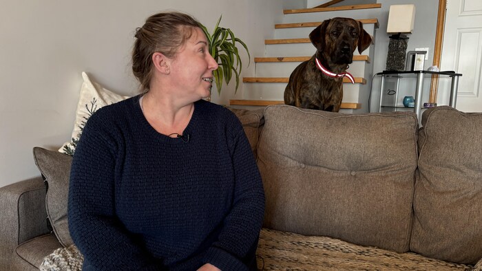 Une femme assise sur un sofa tourne la tête pour regarder un chien.