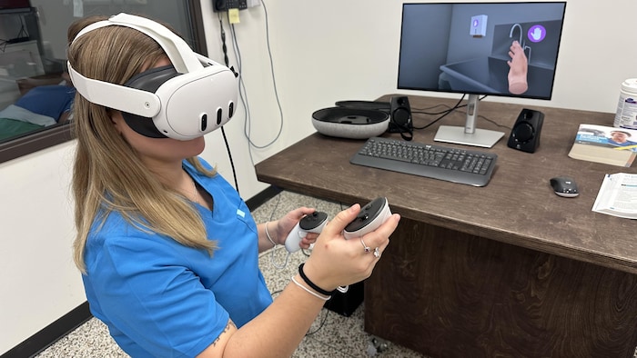 L'étudiante en soins infirmiers pratique ses manipulations à l'aide de manettes et d'un casque de réalité augmentée. 