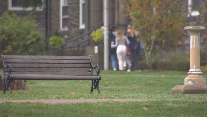 Un banc public sur le campus. À l'arrière, trois personnes floues déambulent devant un bâtiment d'apparence ancienne.