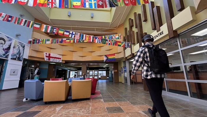 Un corridor de l'Université, un étudiant qui marche, des drapeaux de différents pays accrochés au plafond.