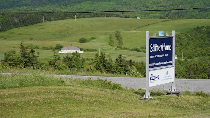 L'enseigne bleue et blanche de l'université plantée dans un décor rural, le long d'une route étroite, dans la verdure.