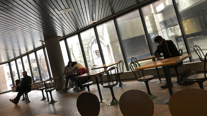 Des personnes assises à des tables dans un grand local vitré.