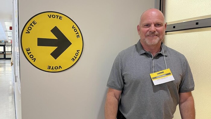 Gino Tremblay, debout devant une affiche qui indique la direction du bureau de vote.
