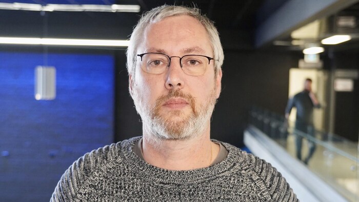 Un homme au visage neutre regarde l'objectif.