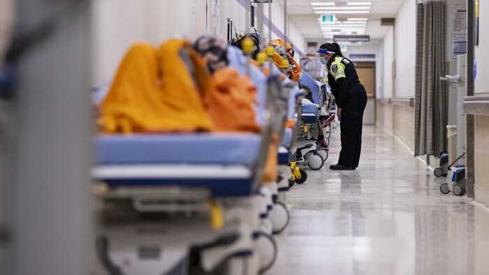 Une ambulancière parle à un patient sur une civière dans le corridor de l'urgence.