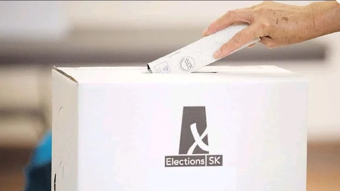 Une main dépose un bulletin de vote dans la fente d'une urne électorale en Saskatchewan.