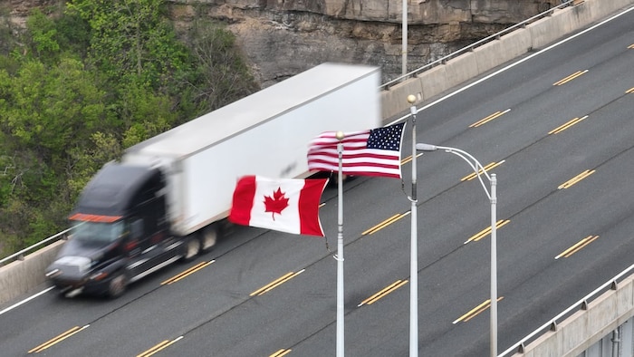 Un camion roule sur une autoroute où flottent les drapeaux américains et canadiens.