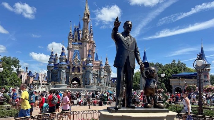 Tourists walk past a statue of Walt Disney and Mickey Mouse at an amusement park.