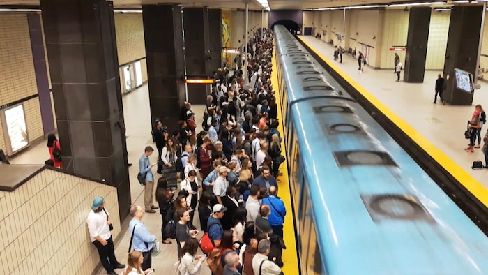 Des usagers sur un quai du métro de Montréal, alors que le train arrive en station.