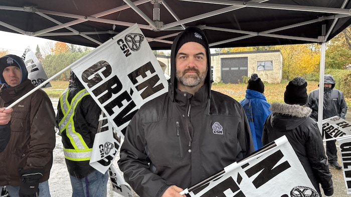 Kevin Lepage accompagné de plusieurs travailleurs avec des pancartes de grève.
