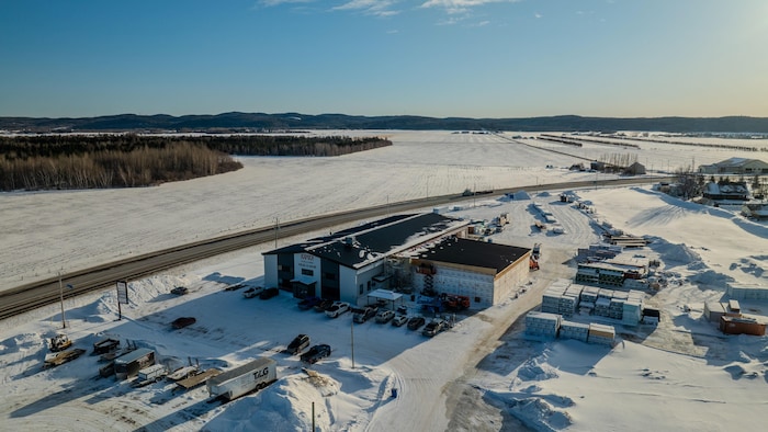 Vue aérienne hivernale d'un bâtiment industriel où une annexe est en construction. Des matériaux de chantier et des véhicules sont visibles autour.