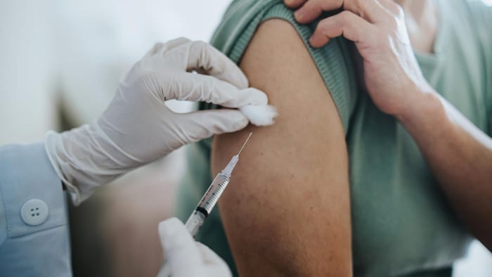 Gros plan sur une femme âgée recevant le vaccin contre la COVID-19 dans le bras, administré par un médecin à l'hôpital.