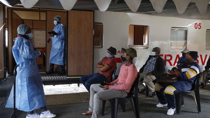 Un travailleur de la santé, debout, s'adresse à des patients assis devant lui lors d'une clinique de vaccination contre la COVID-19 en Afrique du Sud.