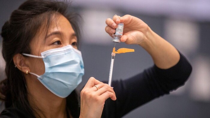 Une femme qui porte un masque sanitaire prépare un vaccin contre la COVID-19. 