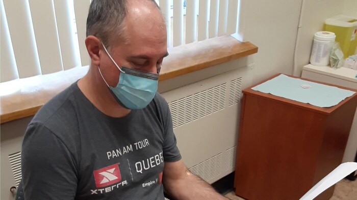 Plan rapproché d'un homme assis dans un bureau de médecin, avec un masque, qui consulte un document. 