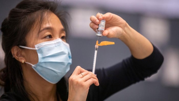 Une femme qui porte le masque sanitaire prépare un vaccin. 