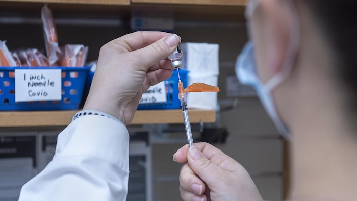 Une pharmacienne extrait le contenu d'un flacon de vaccin à l'aide d'une seringue.
