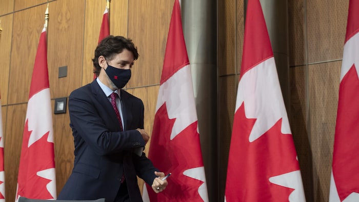 Justin Trudeau porte un masque en marchant devant des drapeaux canadiens.