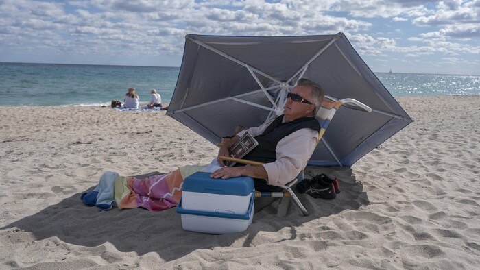 Un homme assis sur la plage sous un parasol.