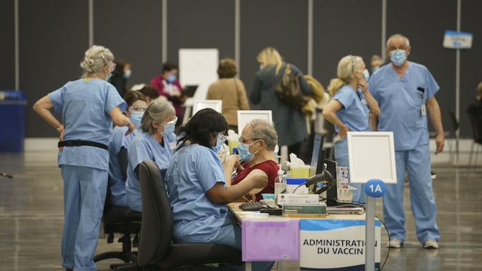 Plusieurs travailleurs de la santé portant des vêtements bleus et des masques sont à pied d'oeuvre dans une salle du Palais de congrès