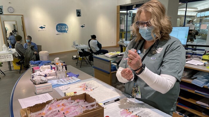 Une infirmière perce une fiole avec la seringue. 