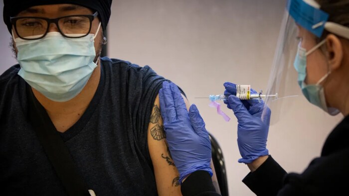 Personal support worker Michael Gellizeau gets a dose of COVID-19 vaccine from nurse practitioner Victoria Pierri at a clinic put on by the University Health Network in Toronto on Dec. 15, 2020.