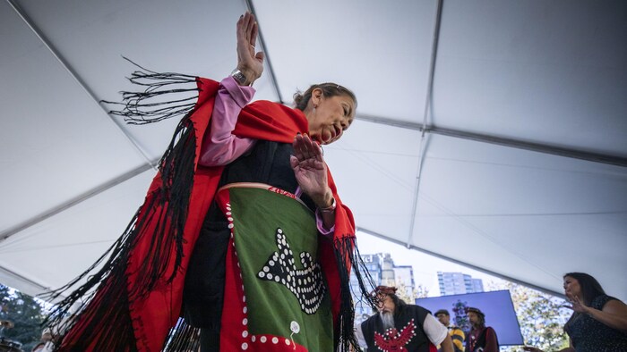 Des femmes et hommes autochtones portant des vêtements traditionnels dansent sous un chapiteau.