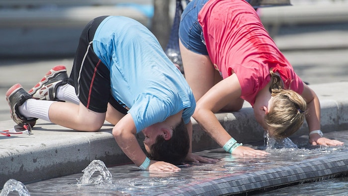 Un garçon et une fille se trempent la tête dans une fontaine pour se rafraîchir.