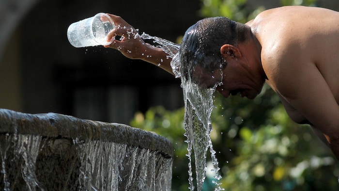 Une personne verse de l'eau d'une fontaine sur sa tête.