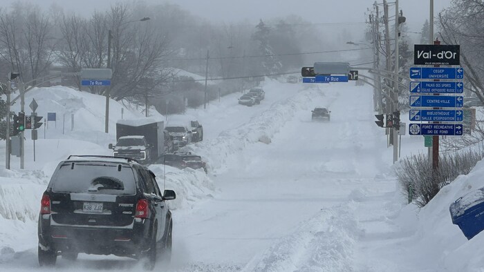 La neige est poussée au centre de la rue. Des voitures circulent.