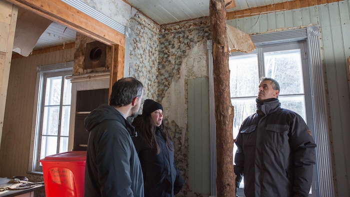 Trois personnes observent l'intérieur d'une maison abandonnée.
