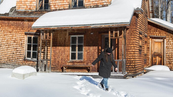 Une dame marche à l'extérieur d'une maison abandonnée.