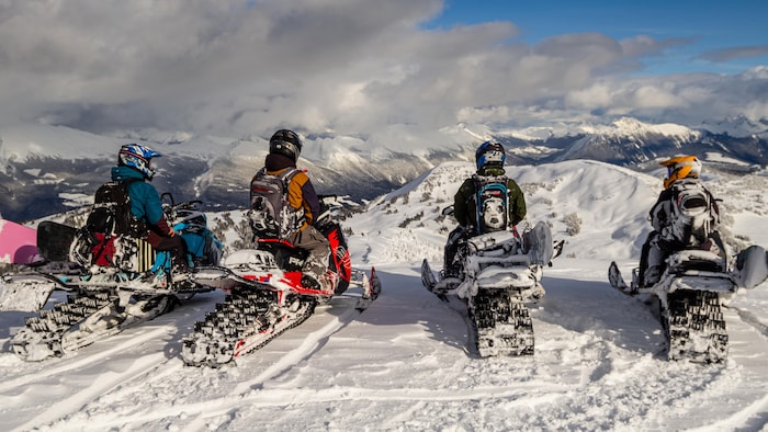 Des motoneigistes en haut d'une montagne.