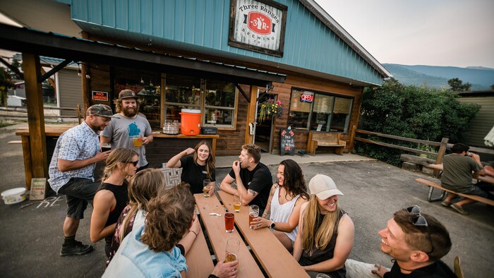 Des personnes autour d'une table de pique-nique devant la brasserie Three Pines Brewing Co., à Valemount.